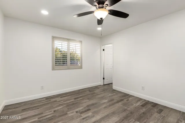 an empty room with wooden floor ceiling fan and windows