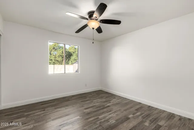 an empty room with wooden floor ceiling fan and window
