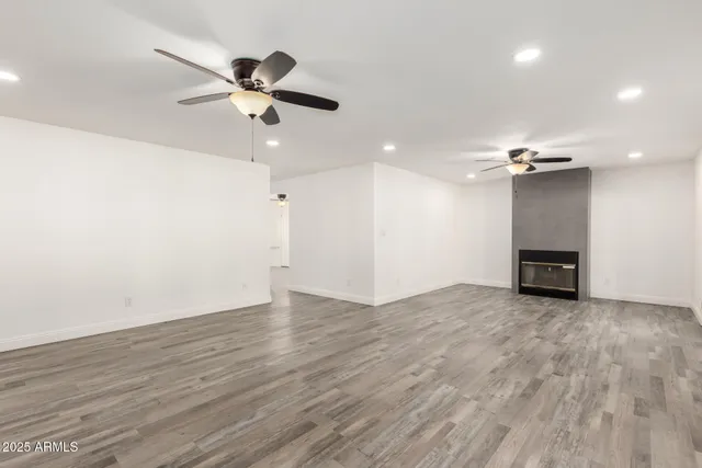 an empty room with wooden floor ceiling fan and windows