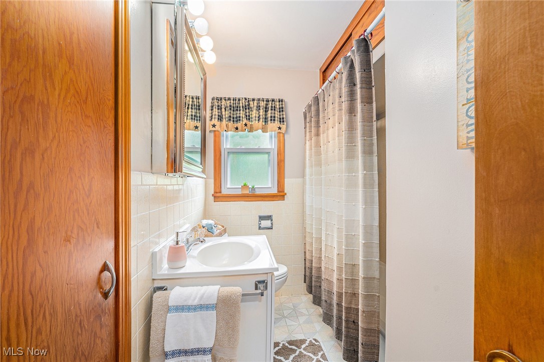 194 Prentice Road Painesville, OH 44077 - Photo 13 of 21 Bathroom featuring vanity, tile walls, tile patterned floors, a wainscoted wall, and a shower with curtain