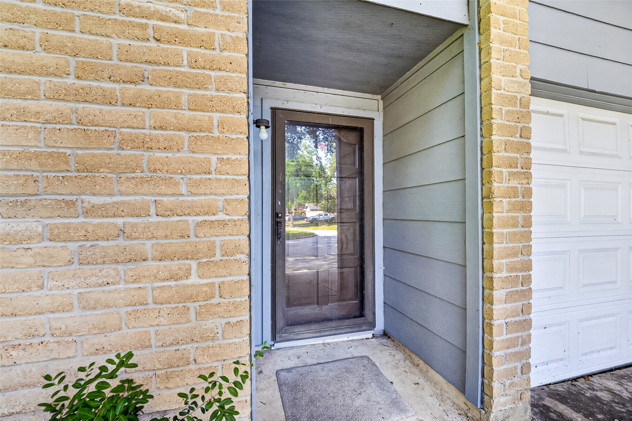 22926 Millgate Drive Spring, TX 77373 - Photo 4 of 34 This photo shows the front entrance of a home with a brick exterior and a glass storm door, leading into a sheltered entryway next to a garage. A small plant adds a touch of greenery.