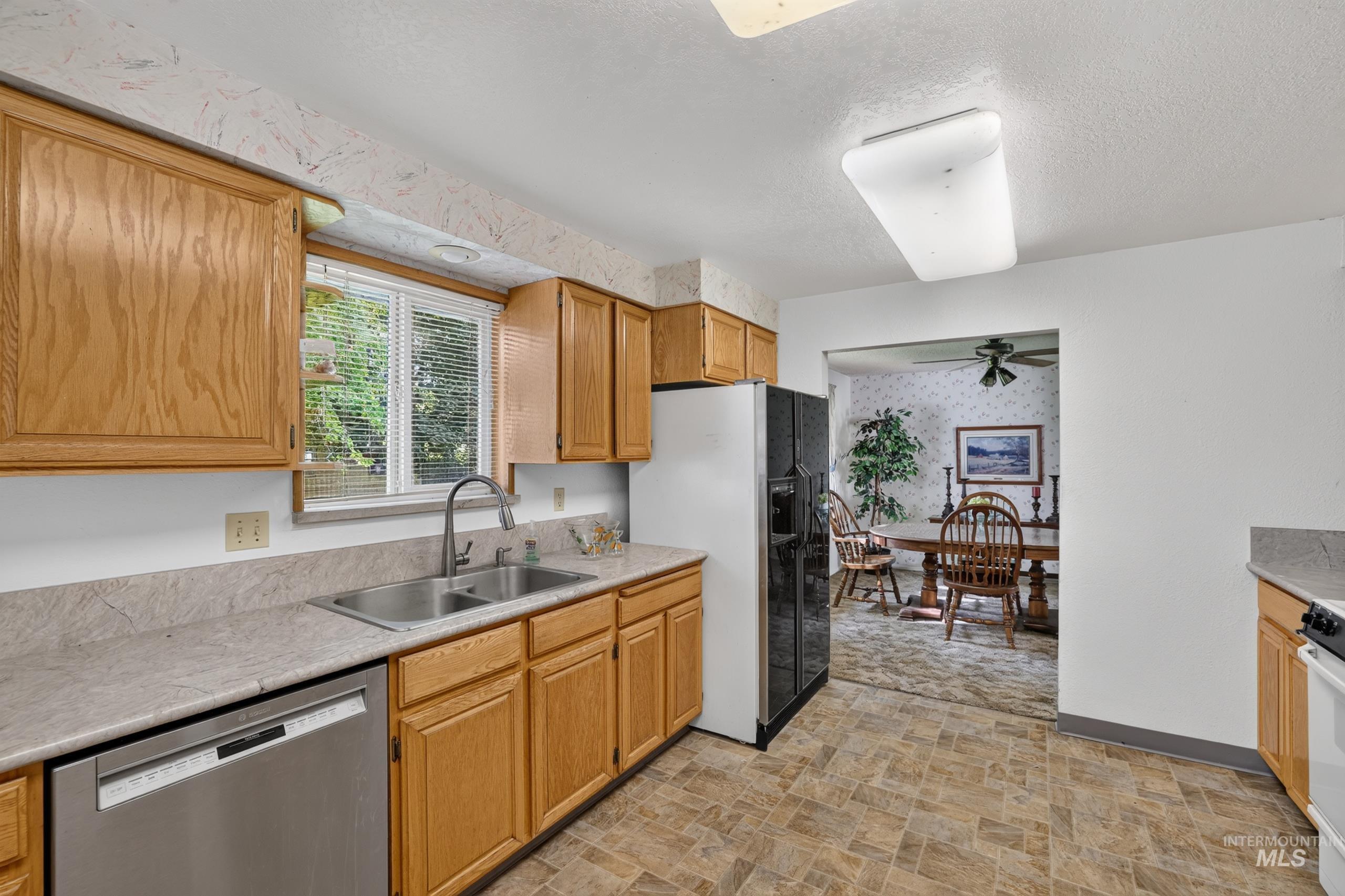 9055 West Highlander Road Boise, ID 83709 - Photo 12 of 39 Kitchen featuring light wood cabinetry, a double basin stainless steel sink, a stainless steel dishwasher, and neutral-toned countertops