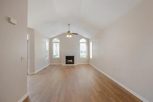 an empty room with wooden floor fireplace and windows