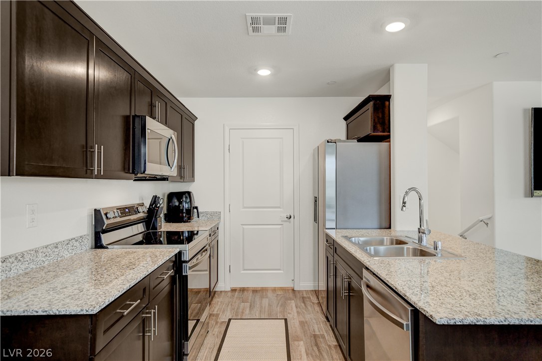 6924 Spicy Merlot Street North Las Vegas, NV 89086 - Photo 16 of 83 A well-appointed kitchen features dark wood cabinetry, light granite countertops, and modern stainless steel appliances.