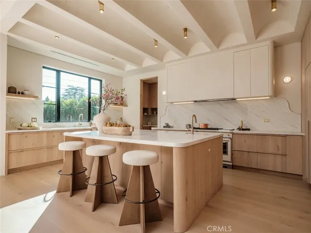 a view of a kitchen with kitchen island a stove a sink a refrigerator and white cabinets with wooden floor