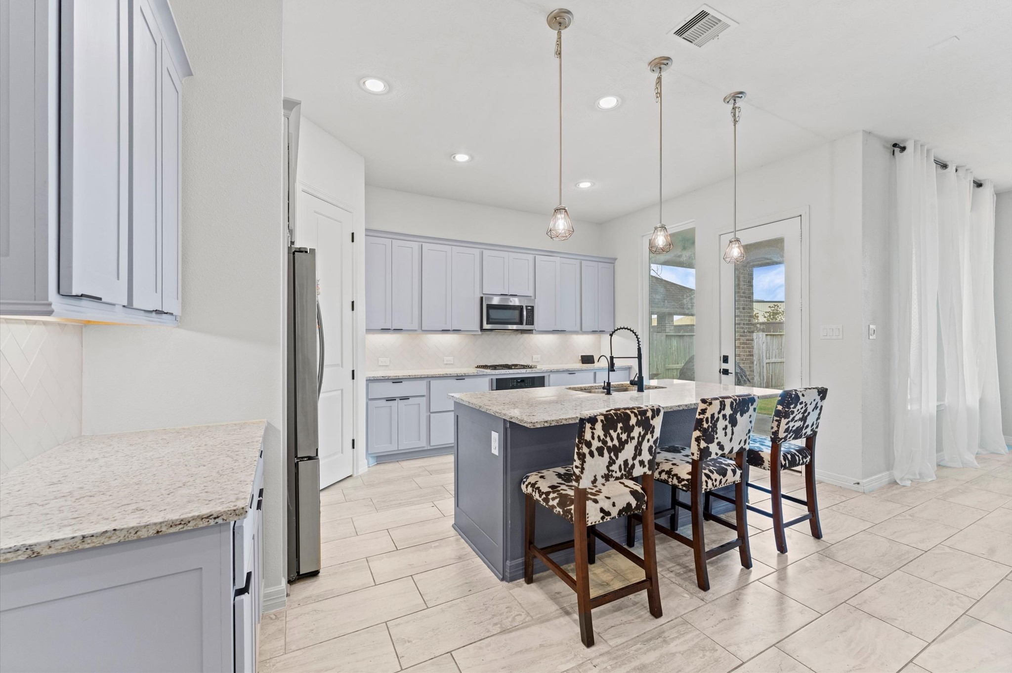 3510 Whitman Drive Rosharon, TX 77583 - Photo 5 of 25 Modern kitchen with light cabinetry, granite countertops, and a spacious island with seating. Features stainless steel appliances, pendant lighting, and tile flooring. Bright and airy with large windows and access to the backyard.