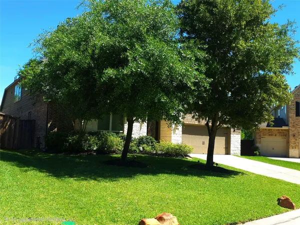a view of a house with a yard plants and large tree