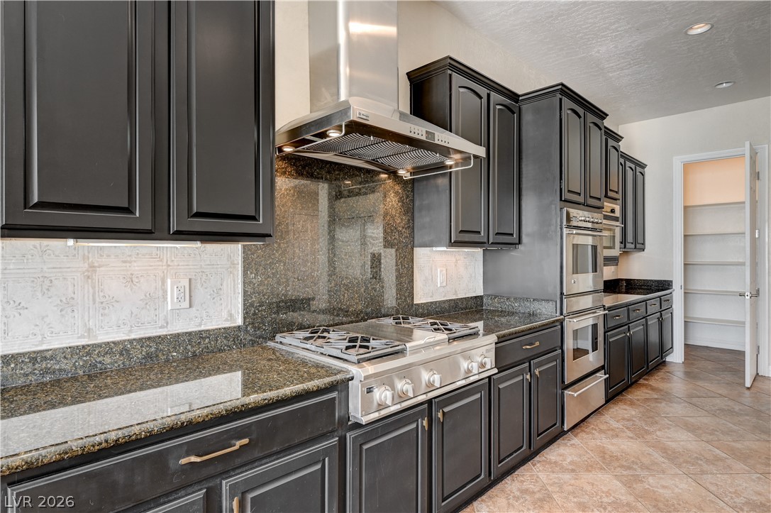 2793 Rosenhearty Drive Henderson, NV 89044 - Photo 25 of 77 An inviting kitchen showcasing sleek dark cabinetry, robust granite countertops, and an array of modern stainless steel appliances.