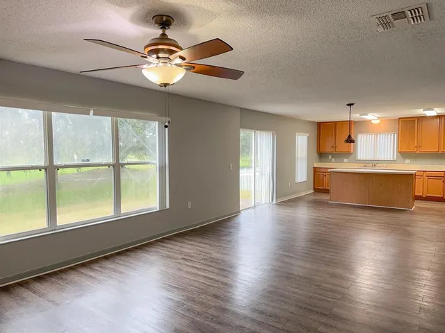 an empty room with wooden floor chandelier fan and windows