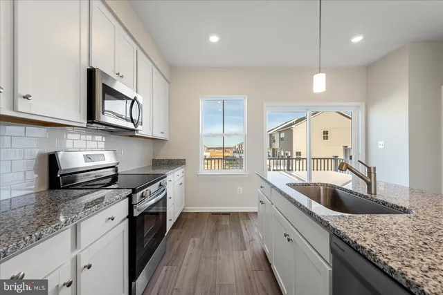 a kitchen with stainless steel appliances granite countertop a refrigerator a sink dishwasher a stove and a large refrigerator with wooden floor