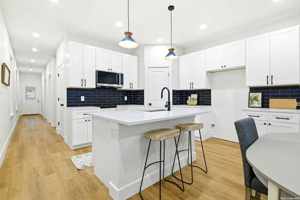 a kitchen with stainless steel appliances a stove a sink a microwave a refrigerator and white cabinets with wooden floor