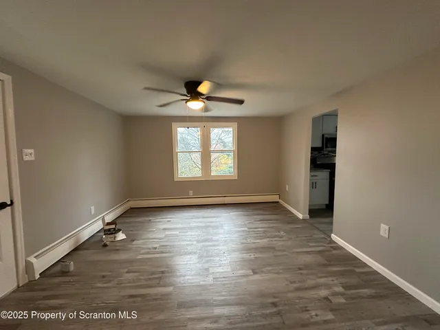 an empty room with wooden floor chandelier fan and windows