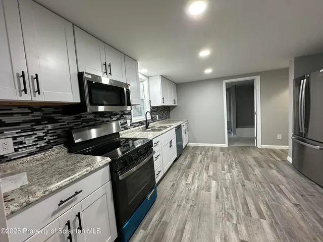 a kitchen with granite countertop a stove top oven a sink dishwasher a refrigerator and cabinets with wooden floor