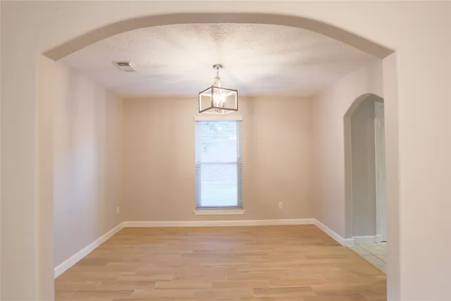 an empty room with wooden floor chandelier and windows