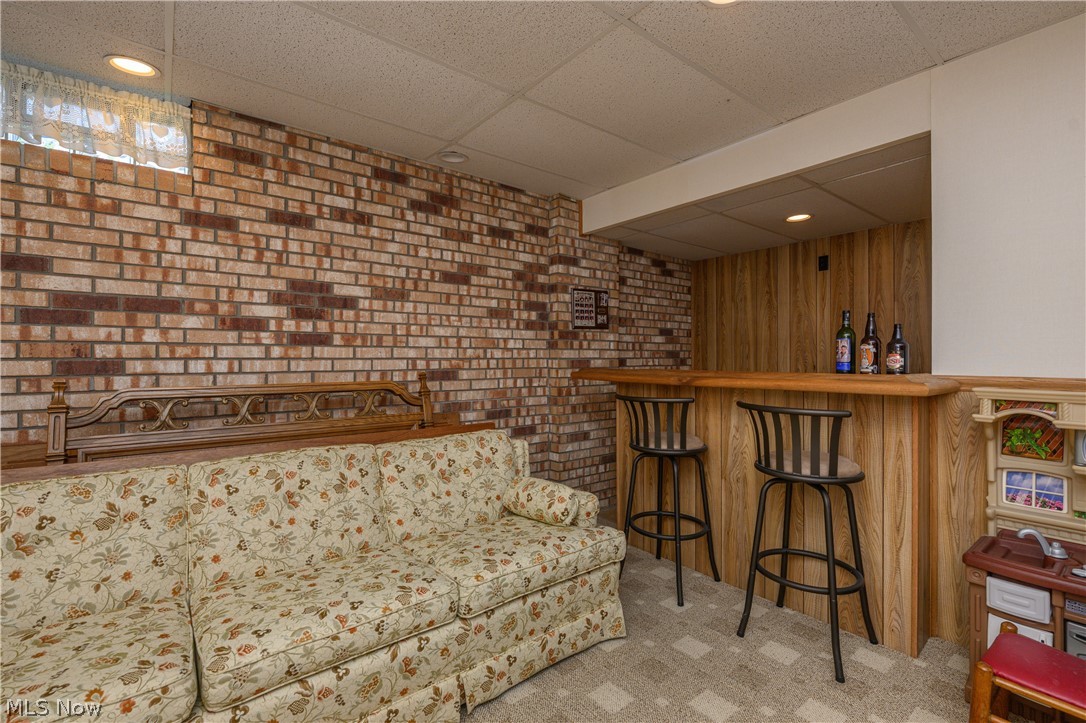 3281 Brenner Road Barberton, OH 44203 - Photo 32 of 33 Living room featuring bar, wooden walls, brick wall, light carpet, and a paneled ceiling