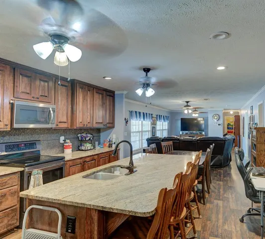 a kitchen with stainless steel appliances granite countertop a stove top oven a sink a dining table and chairs with wooden floor