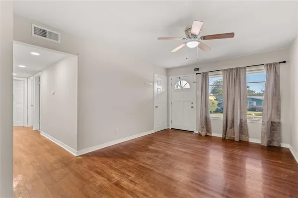 a view of an empty room with wooden floor and a ceiling fan
