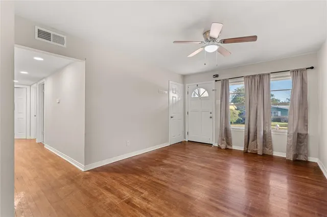 a view of an empty room with wooden floor and a ceiling fan