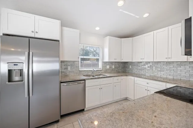 a kitchen with stainless steel appliances granite countertop a refrigerator a sink and white cabinets