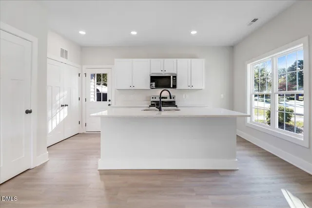 a view of kitchen with stainless steel appliances granite countertop a stove a sink a refrigerator and white cabinets with wooden floor
