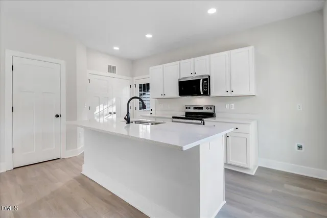 a kitchen with kitchen island granite countertop a sink a stove a microwave a refrigerator a counter top space and cabinets