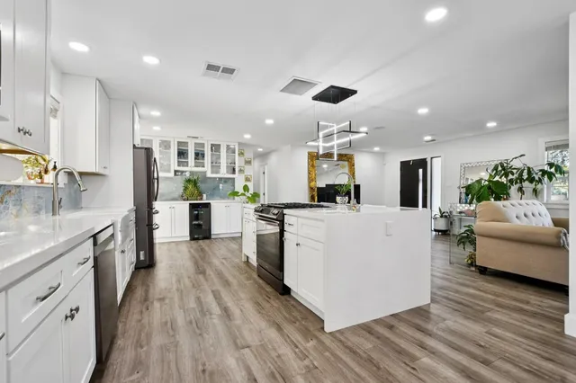 a large white kitchen with stainless steel appliances kitchen island a stove a refrigerator a couch and a dining table with wooden floor