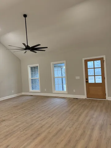 a view of an empty room with wooden floor ceiling fan and windows