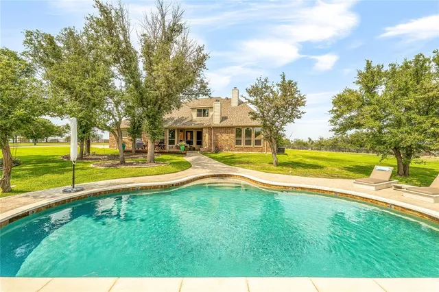 a view of swimming pool with lawn chairs and large trees