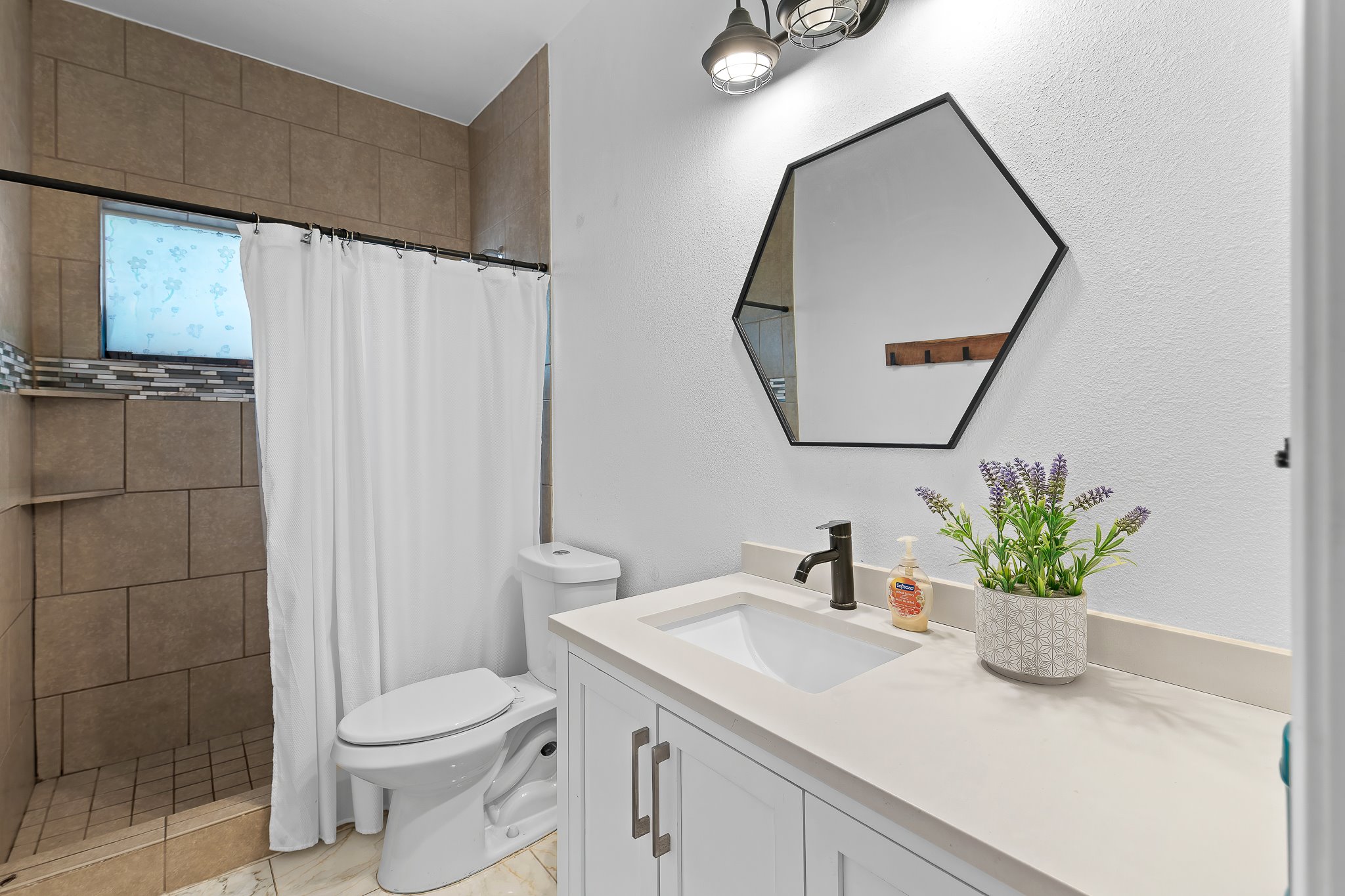 11737 Rydalwater Lane Austin, TX 78754 - Photo 14 of 40 Bathroom featuring a white vanity with integrated sink, a dark bronze faucet, and a hexagonal mirror