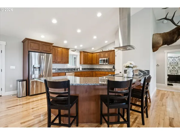 a kitchen with stainless steel appliances kitchen island granite countertop a dining table chairs and a refrigerator