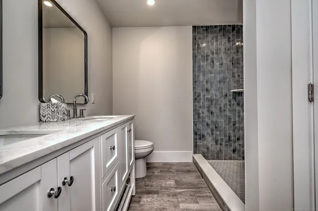 a bathroom with a granite countertop sink a toilet a mirror and shower