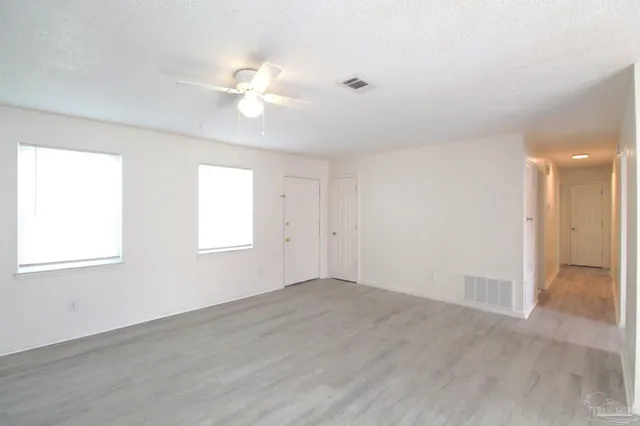 an empty room with wooden floor fan and windows