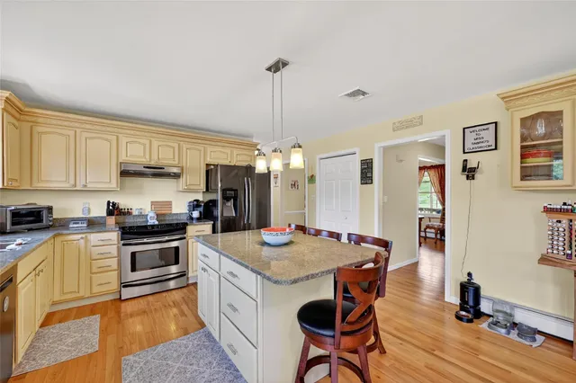 a kitchen with stainless steel appliances granite countertop a stove top oven a sink a dining table and chairs with wooden floor