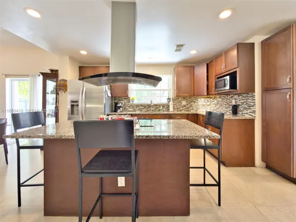 a kitchen with stainless steel appliances kitchen island granite countertop a table chairs sink and cabinets