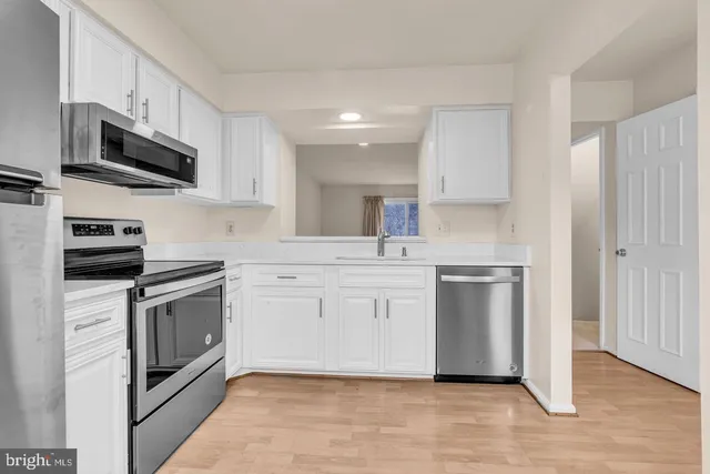 a kitchen with stainless steel appliances white cabinets a sink a stove a microwave and wooden floors