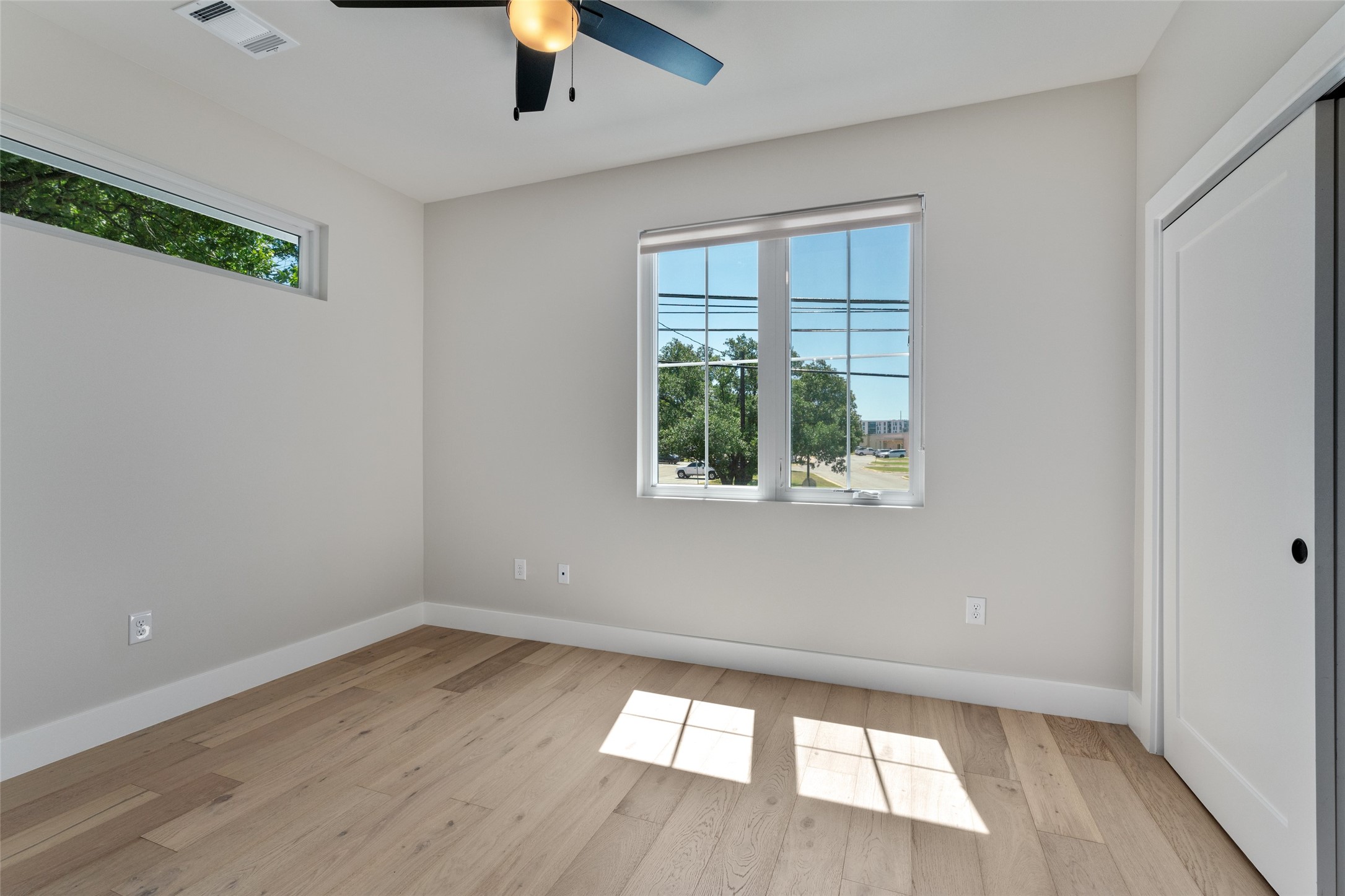 5200 Grover Avenue Austin, TX 78756 - Photo 22 of 32 Light and airy secondary bedroom featuring wood-finish flooring, a large window with white framing, a high horizontal window, and a ceiling fan with integrated lighting. This secondary bedroom features a full bathroom.