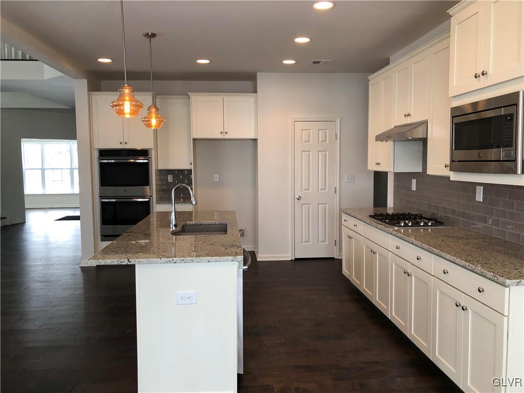 6559 Gun Club Road, Unit 35 Coopersburg, PA 18036 - Photo 21 of 48 a kitchen with kitchen island granite countertop a stove a sink a refrigerator and white cabinets with wooden floor