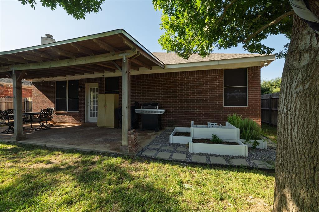 4025 Chisos Rim Trail Fort Worth, TX 76244 - Photo 37 of 40 Brick exterior featuring a covered patio with exposed wood beams, a concrete patio surface, a glass-paned door, and tiered raised garden beds