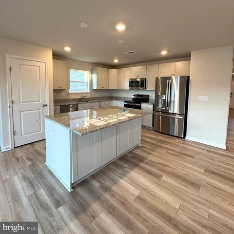 a kitchen with stainless steel appliances granite countertop a refrigerator oven a sink dishwasher and white cabinets with wooden floor