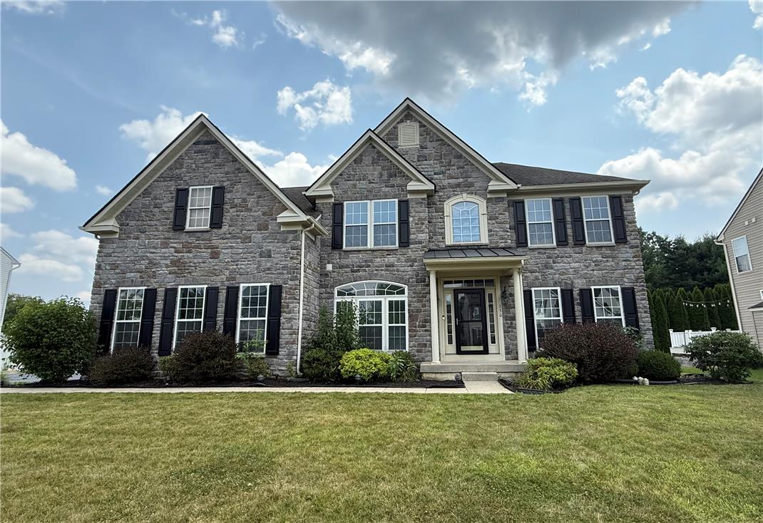 A grand two-story stone facade welcomes you to this distinguished residence, featuring classic shutters and an inviting entryway.