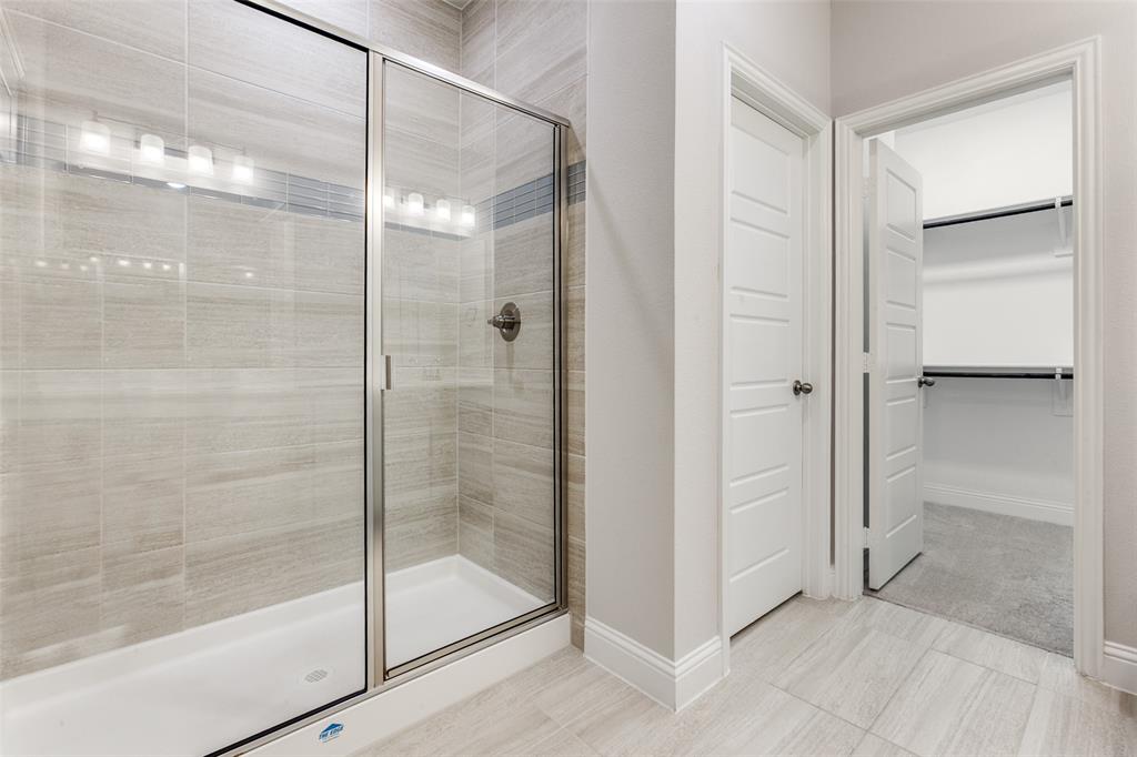 1888 Strand Street Dallas, TX 75234 - Photo 10 of 13 Shower with glass enclosure, light-toned tile walls featuring a decorative accent band, and a brushed nickel shower fixture