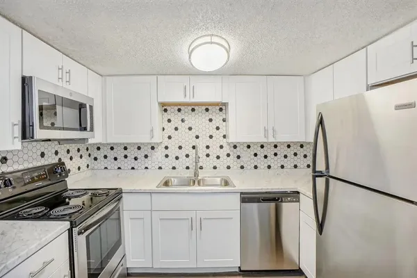 a kitchen with granite countertop a refrigerator stove and white cabinets