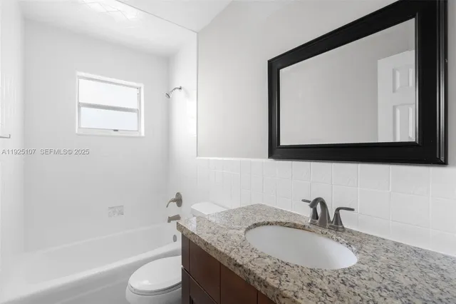 a bathroom with a granite countertop toilet a sink a mirror and bathtub