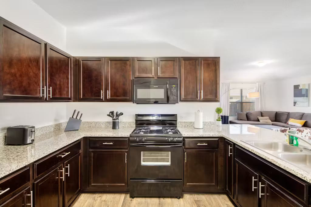 3609 Batson Drive Austin, TX 78725 - Photo 32 of 33 Kitchen with black appliances, light wood finished floors, open floor plan, dark brown cabinets, and light stone counters