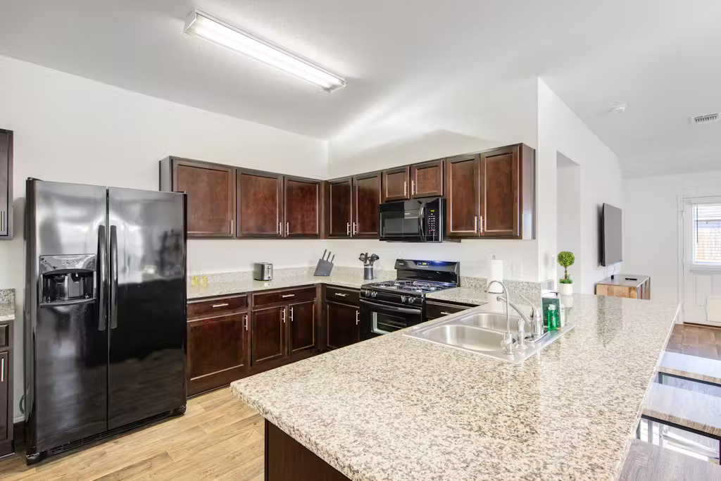 3609 Batson Drive Austin, TX 78725 - Photo 28 of 33 Kitchen with dark brown cabinetry, black appliances, light wood-style flooring, a peninsula, and light stone counters