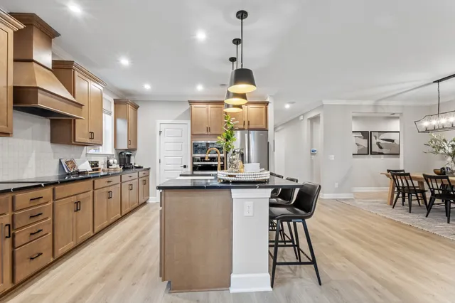 a kitchen with stainless steel appliances granite countertop a stove top oven a sink a dining table and chairs with wooden floor