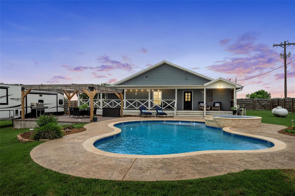 Pool at dusk with a patio area, a pool with connected hot tub, area for grilling, and a pergola