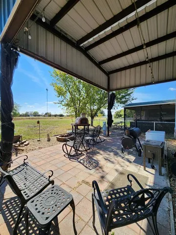 a view of a patio with table and chairs under an umbrella with a barbeque