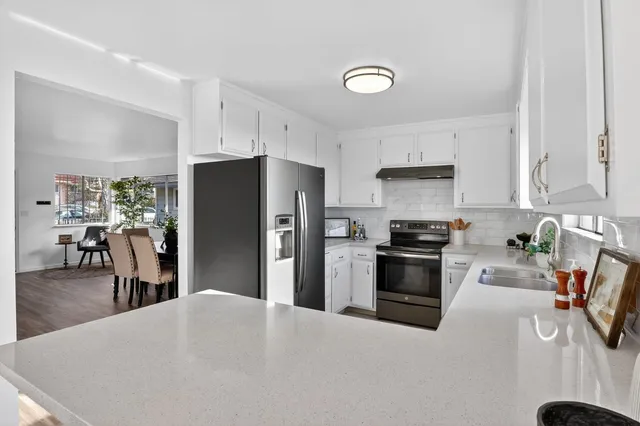 a kitchen with stainless steel appliances kitchen island granite countertop a refrigerator a stove a sink a dining table and chairs with wooden floor