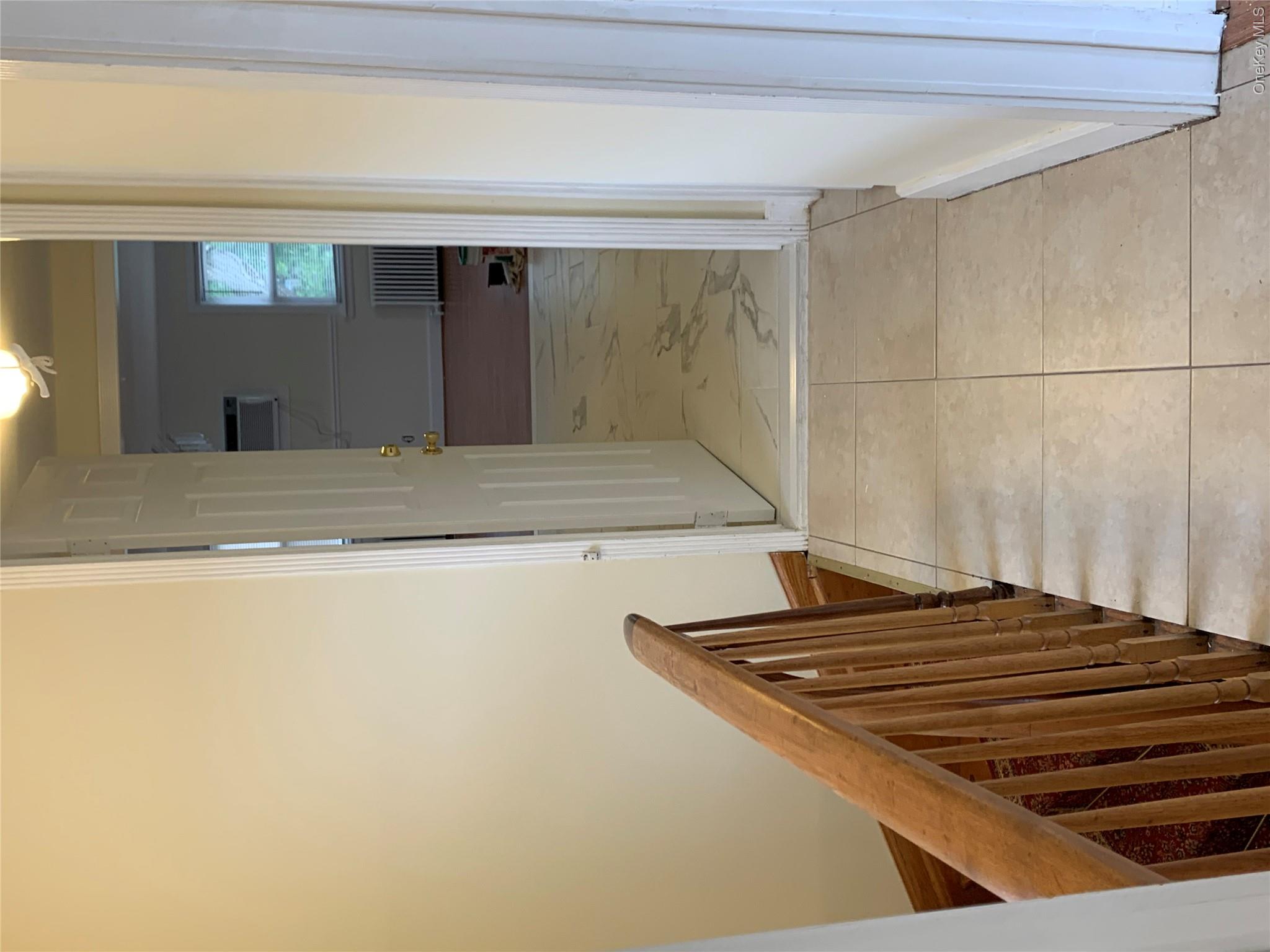 7 Clinton Street Haverstraw, NY 10927 - Photo 8 of 20 Hallway featuring light-toned tile flooring, a wood baluster railing, and a doorway opening to a room with wood-finish flooring and a window